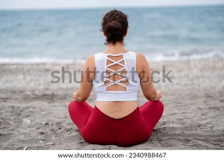 Beautiful lady meditation in lotus pose doing yoga at the beach backwards