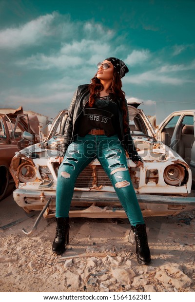 Beautiful\
lady posing beside old rusty car in\
junkyard