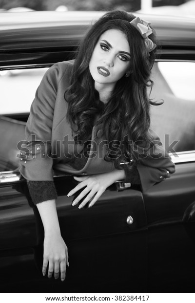 Beautiful lady sitting in a retro car.\
Black and white. Brunette hair style. Fashion\
portrait.