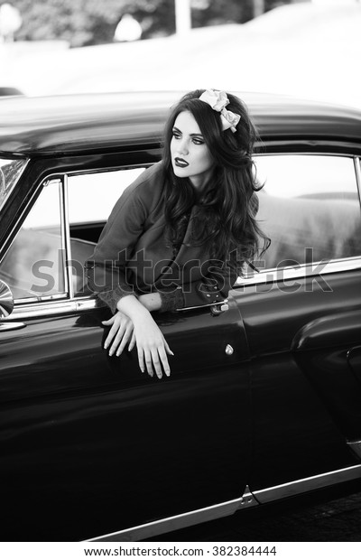 Beautiful lady sitting in a retro car.\
Black and white. Brunette hair style. Fashion\
portrait.
