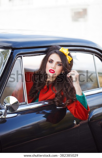 Beautiful lady sitting in a retro car. Red\
lips. Brunette hair style. Fashion\
portrait.