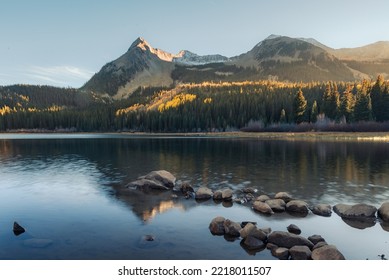 A beautiful lake scene looking across at a mountain landscape. The fall sunset casts light on the mountain peak behind the lake. The image is a long exposure, creating a milky and smooth lake water  - Shutterstock ID 2218011507