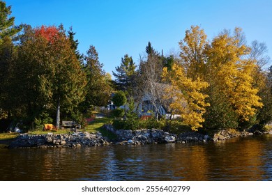 A beautiful lakefront cottage captures the essence of autumn with vibrant foliage reflecting on the water. Ideal for relaxation and appreciating nature's beauty in a serene, peaceful setting. - Powered by Shutterstock