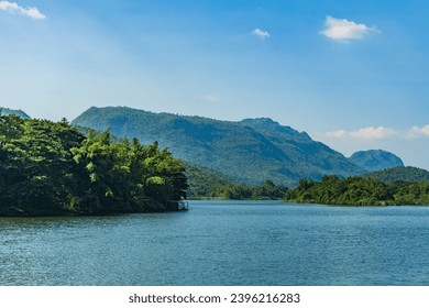 Beautiful lakeside view from a small lake in Kanchanaburi Thailand, with green trees, blue sky and sunlight - Powered by Shutterstock