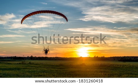 Beautiful landscape with back view of paramotor pilot over rural meadow during sunset