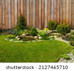  A beautiful landscape of the backyard and a composition of flowers and bushes against the background of a wooden fence. Detail of the botanical garden.