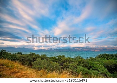Beautiful landscape with colorful dramatic sunset clouds over the Sevan lake in Armenia with green bushes on foreground. Wide angle view