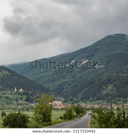 Beautiful landscape, countryside scenery of a rural sight, hills in dramatic clouds on background. Road towards Shipka town, Balkan Mountains, Bulgaria. Travel and nature concept.