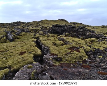 Beautiful landscape with deep rocky fissure on volcanic lava field covered by green moss and lichens near Grindavik, Reykjanes peninsula, Iceland on cloudy winter day.