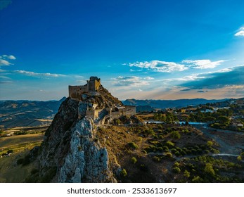 A beautiful landscape featuring a historic castle atop a rocky hill under a clear blue sky during sunset. - Powered by Shutterstock