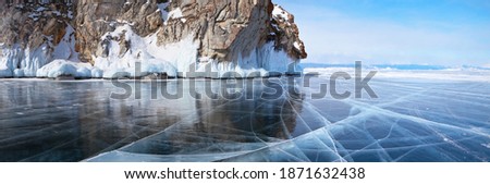 Beautiful landscape of frozen Lake Baikal on a sunny February day. A panoramic view of the icy cliffs of Olkhon Island and clear transparent ice with cracks. Winter holidays, ice travel