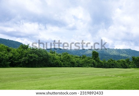 Beautiful landscape of golf course with greenery fairway field. Scenery of rich green turf and lush foliage trees alongside giant mountain covered by a vast white cloudy sky. Beauty of nature and land