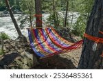 Beautiful landscape with hammock in the summer sunny day. Against the background of a mountain river.
A gently swinging hammock tied between two trees. Concept for relaxation, rural tourism.