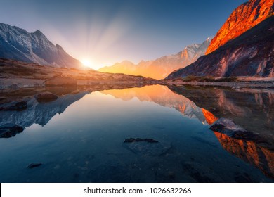 Красивый пейзаж с высокими горами с освещенными вершинами, камни в горном озере, отражение, голубое небо и желтый солнечный свет на восходе солнца. Непал. Удивительная сцена с гималайских гор. Гималаи