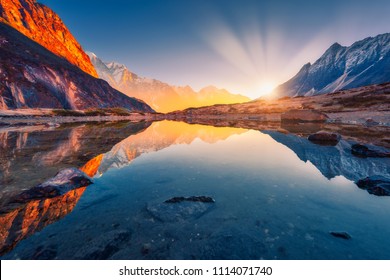 Beautiful landscape with high mountains with illuminated peaks, stones in mountain lake, reflection, blue sky and yellow sunlight in sunrise. Nepal. Amazing scene with Himalayan mountains. Himalayas - Powered by Shutterstock