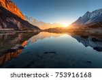 Beautiful landscape with high rocks with illuminated peaks, stones in mountain lake, reflection, blue sky and yellow sunlight in sunrise. Nepal. Amazing scene with Himalayan mountains. Himalayas