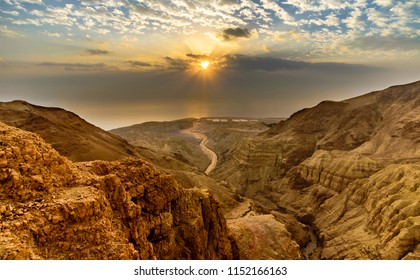 Beautiful landscape of Israeli Judean Desert mountains, with sunrise over the dry riverbed of Nahal Dragot Wadi, popular hiking trail winding between rugged rocky cliffs towards the Dead Sea