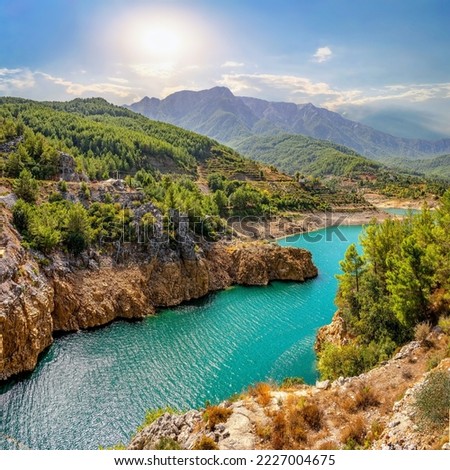 Beautiful landscape of mountainous nature with bright summer sun, blue sky, high mountains, green hills, yellow rocks and turquoise water lake.