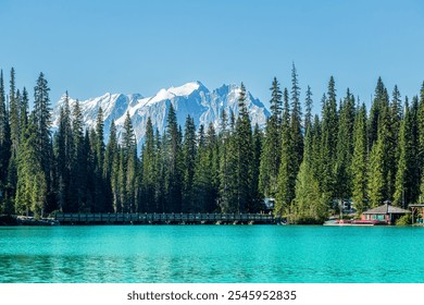 A beautiful landscape photo of Emerald Lake with canoes and a boathouse, a bridge to the lodge, an evergreen forest, and snow-capped mountains on a clear blue sky day. Yoho National Park, British Col - Powered by Shutterstock