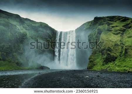 Beautiful landscape of powerful Skogafoss waterfall with Skoga river flowing from cliff in summer on gloomy day at Iceland