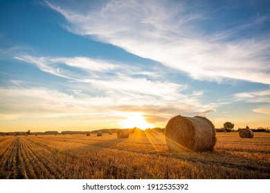 Beautiful landscape of setting sun over a big agricultural field of straw rolled into bales. Rural scenery - Shutterstock ID 1912535392