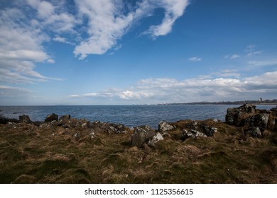 Beautiful landscape with vegetation, sand shore, North Sea and dramatic blue cloudy sky. View from Cramond island, Cramond beach, Edinburgh, Scotland