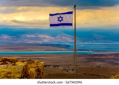 Beautiful Landscape View From Masada Fortress Overlooking The Dead Sea And Jordan Mountains; The Flag Of Israel With Its Blue Star Of David (Magen David) In The Foreground Against A Cloudy Sky