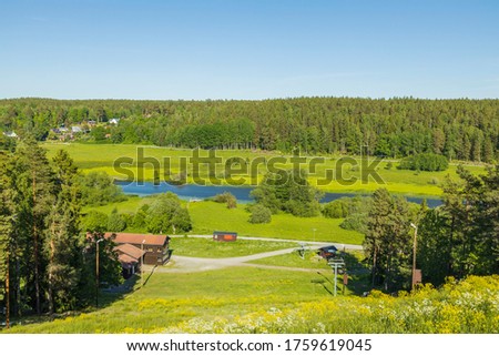 Beautiful landscape view on summer day. Private wooden houses between green forest trees. Small river along asphalt road. 