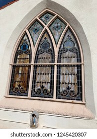 Beautiful Large Stained Glass Window On Mission Style Church With Small Madonna Statue On The Ground