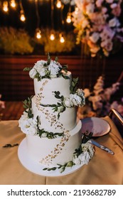 A Beautiful Large Three-tier White, Decorated With Rose Flowers, Cream Wedding Cake Stands On The Table In The Evening. Food Photography.