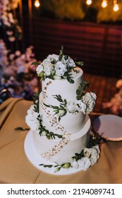 A Beautiful Large Three-tier White, Decorated With Rose Flowers, Cream Wedding Cake Stands On The Table In The Evening. Food Photography.