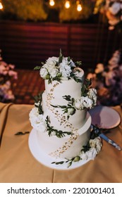 A Beautiful Large Three-tier White, Decorated With Rose Flowers, Wedding Creamy Sweet Cake Stands On The Table In The Evening. Food Photography.