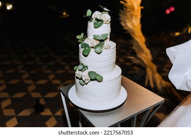 A Beautiful, Large, Three-tiered Cake Decorated With Flowers Stands On The Table At A Party At Night. Wedding Food Photography.