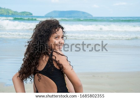 Beautiful latin american girl smiling sitting on a rock at the beach looking beyond