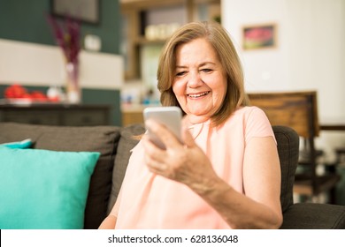 Beautiful Latin Grandmother Using Her Smartphone To Watch A Video Sitting At Home