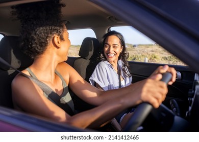 Beautiful Latin Hispanic Woman With Friend Enjoying And Laughing In Car While Going On A Road Trip. Cheerful Girl Friends Enjoying Trip And Drive In Car At Sunset. Black Woman Driving A Car.