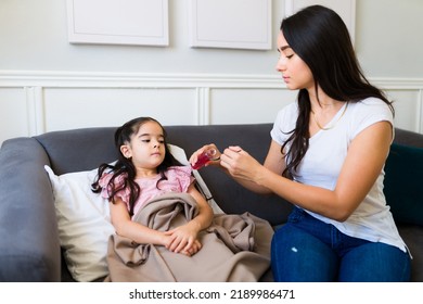 Beautiful Latin Mom Giving Cough Syrup And Medicine To Her Sick Youg Child Suffering From A Bad Cold