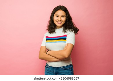 Beautiful latin teen girl smiling wearing casual clothes looking happy against a pink studio background