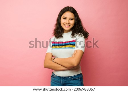 Beautiful latin teen girl smiling wearing casual clothes looking happy against a pink studio background