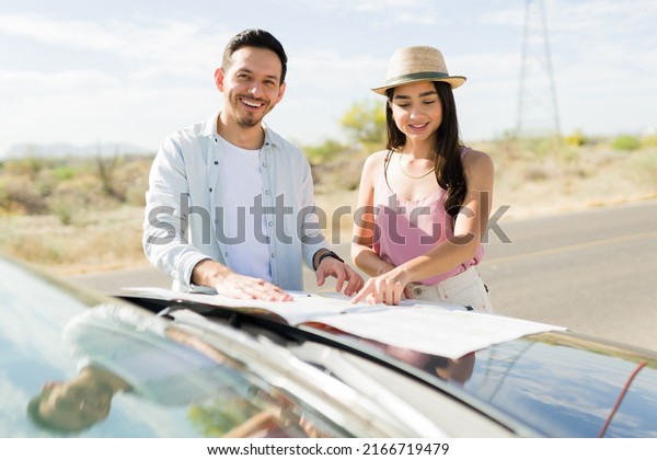 Beautiful latin woman and happy young\
man checking a road map while driving for a vacation\
trip