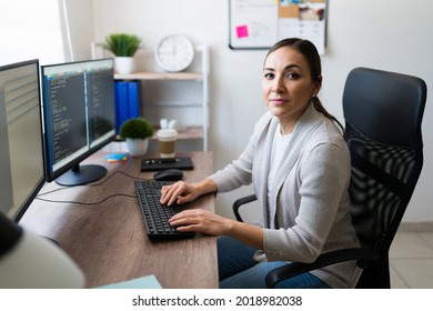 Beautiful Latin Woman Making Eye Contact While Typing On The Computer And Writing Code. Professional Woman Working As A Programmer Freelancer 