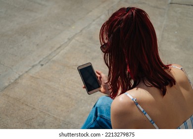 Beautiful Latin Woman With Red Hair Looking At Her Cell Phone. Copy Space. Landscape Orientation.