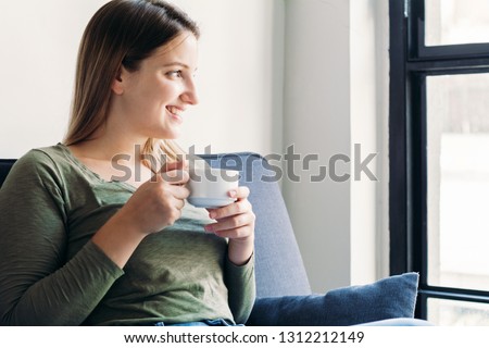 Beautiful latin woman relaxing on couch and enjoying cup of coffee at home. Indoors        
