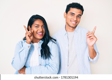 Beautiful Latin Young Couple Wearing Casual Clothes With A Big Smile On Face, Pointing With Hand And Finger To The Side Looking At The Camera. 