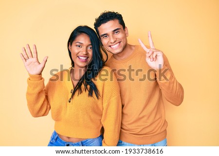 Beautiful latin young couple wearing casual clothes together showing and pointing up with fingers number seven while smiling confident and happy. 