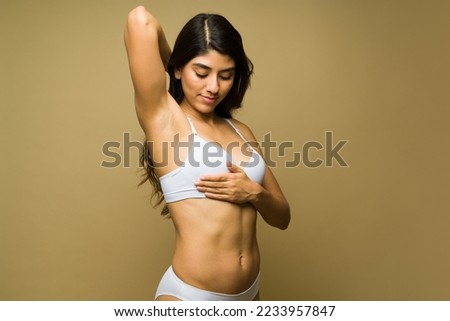 Beautiful latin young woman in underwear raising her arm and doing a breast self examination to prevent cancer