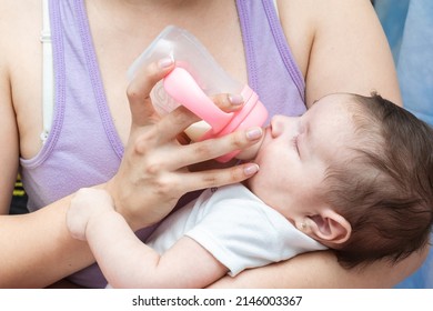 beautiful latina baby girl drinking from a bottle with her eyes closed while being held in her mother's arms. two month old baby girl drinking milk from a pink bottle.