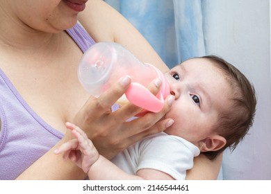 beautiful latina baby with her eyes open while taking the bottle her mother is giving her to calm her hunger. baby about to fall asleep with a sleepy face.