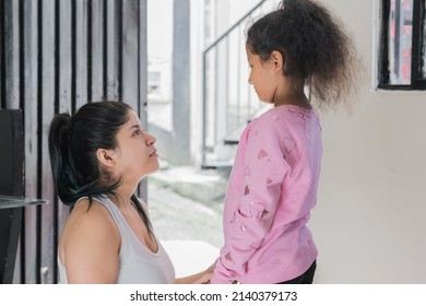 beautiful latina mother sitting on the floor while looking her brown-skinned daughter in the eyes, the girl is standing next to her mother who advises her and is proud of her. family concept