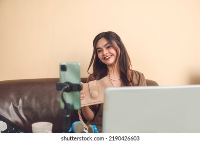 Beautiful Latina Online Selling Her Mini Hand Bag Doing Live Feed With Phone As Camera Video Laptop As Foreground